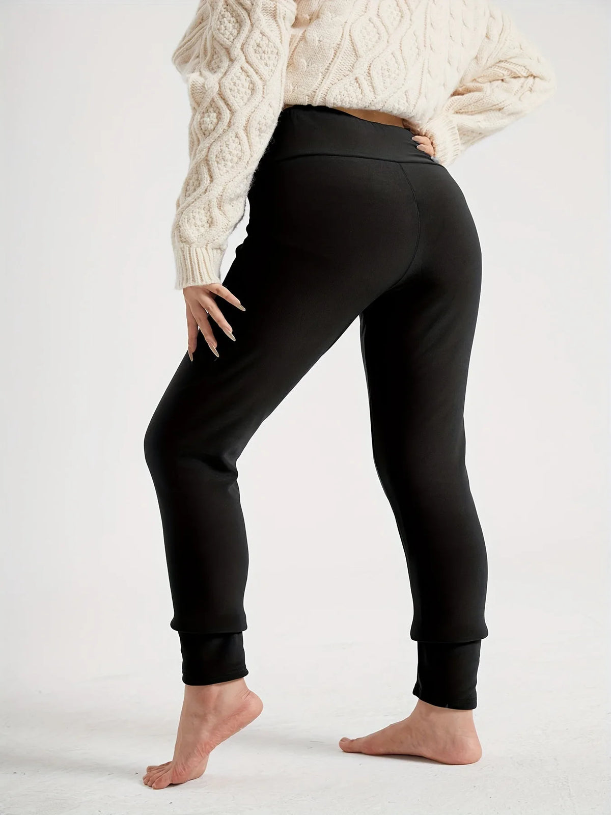 Back view of a woman wearing black high-waist fleece-lined leggings with a cream cable-knit jumper