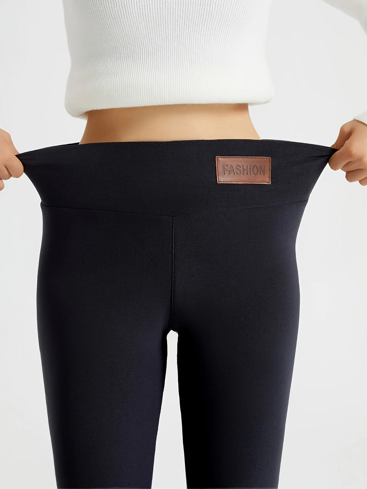 Close-up front view of black leggings waistband stretched wide, showing brown fabric patch labelled Fashion