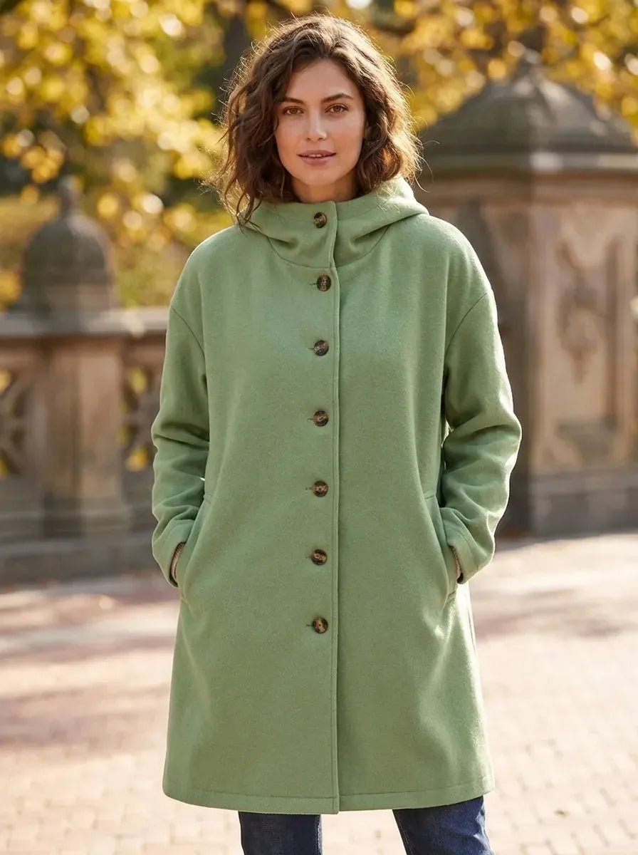 Front view of a woman wearing a sage green hooded wool-blend coat with tortoiseshell buttons over jeans