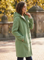 Side profile of the sage green hooded coat worn open, hand raised to the hood edge