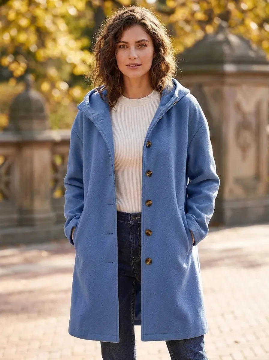 Model wearing the same hooded longline coat in a soft denim blue shade over a cream jumper