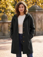 Model wearing the hooded longline coat in a deep forest green shade, fully buttoned up