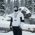 Man modelling white and black hooded ski anorak with goggles and beanie beside a snowy riverbank