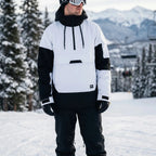 Man wearing a white and black colourblock hooded ski anorak with goggles, standing on a snowy slope with mountains behind