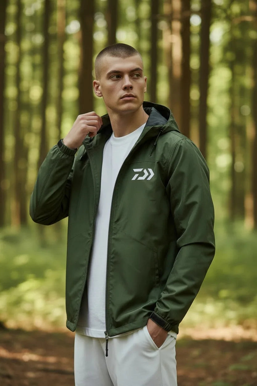 Man in a forest wearing an open khaki green hooded jacket over a white t-shirt, holding the collar.