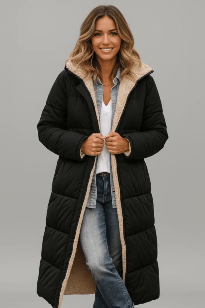Smiling woman wearing a black hooded longline puffer coat with beige sherpa lining, worn open over denim shirt and jeans