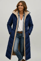 Woman wearing a navy blue quilted longline coat with hood down, open over a denim shirt and belted jeans