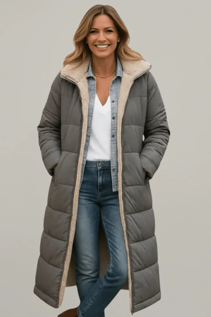 Woman wearing a grey longline puffer coat with beige fleece trim, hands in pockets, styled with jeans