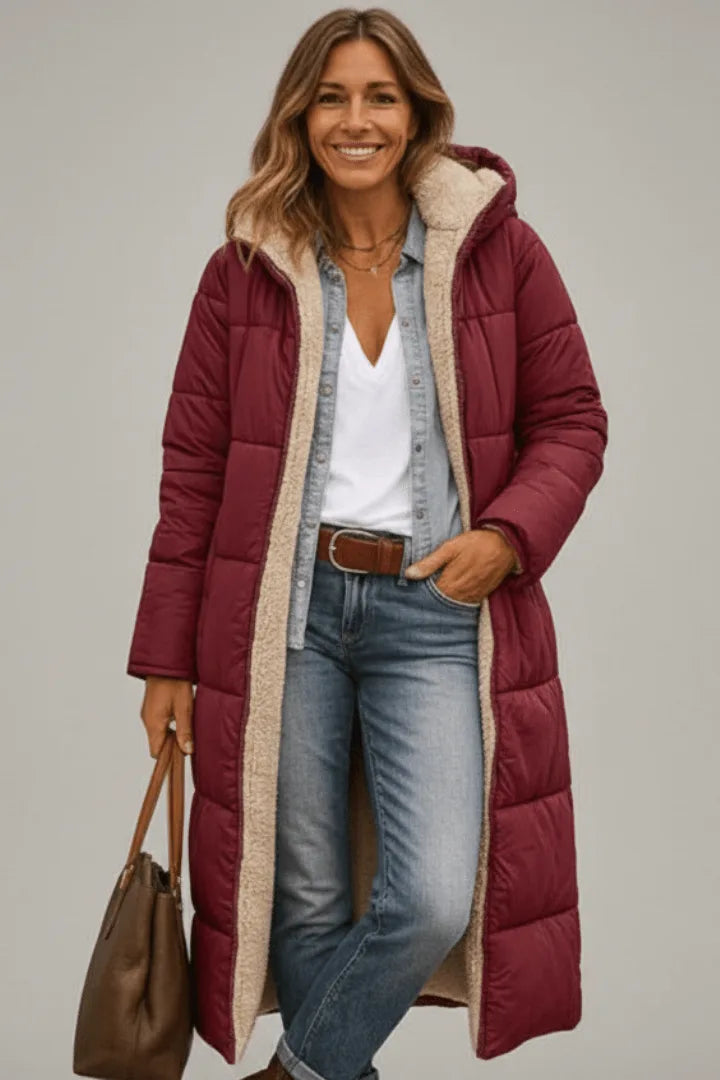 Woman wearing a burgundy hooded longline puffer coat with beige fleece lining, carrying a brown handbag