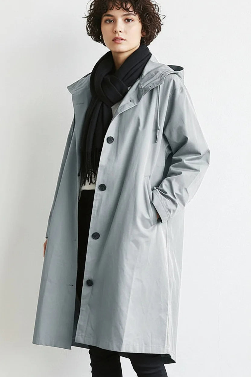 Front view of a light grey hooded longline trench coat worn open over a black jumper and dark trousers