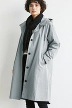 Front view of a light grey hooded longline trench coat worn open over a black jumper and dark trousers