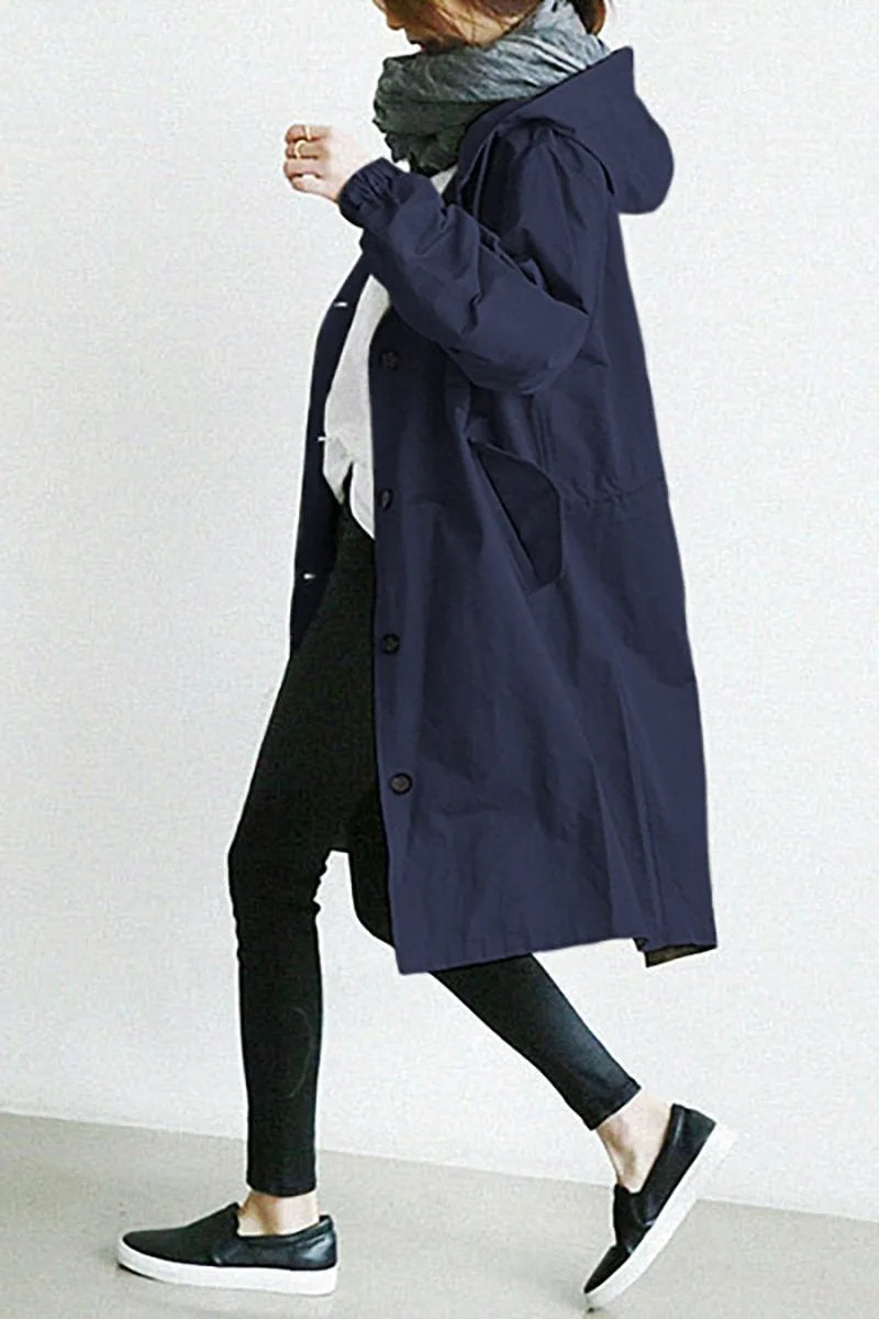 Side profile of a navy blue hooded trench coat worn while walking, showing elastic cuff detail