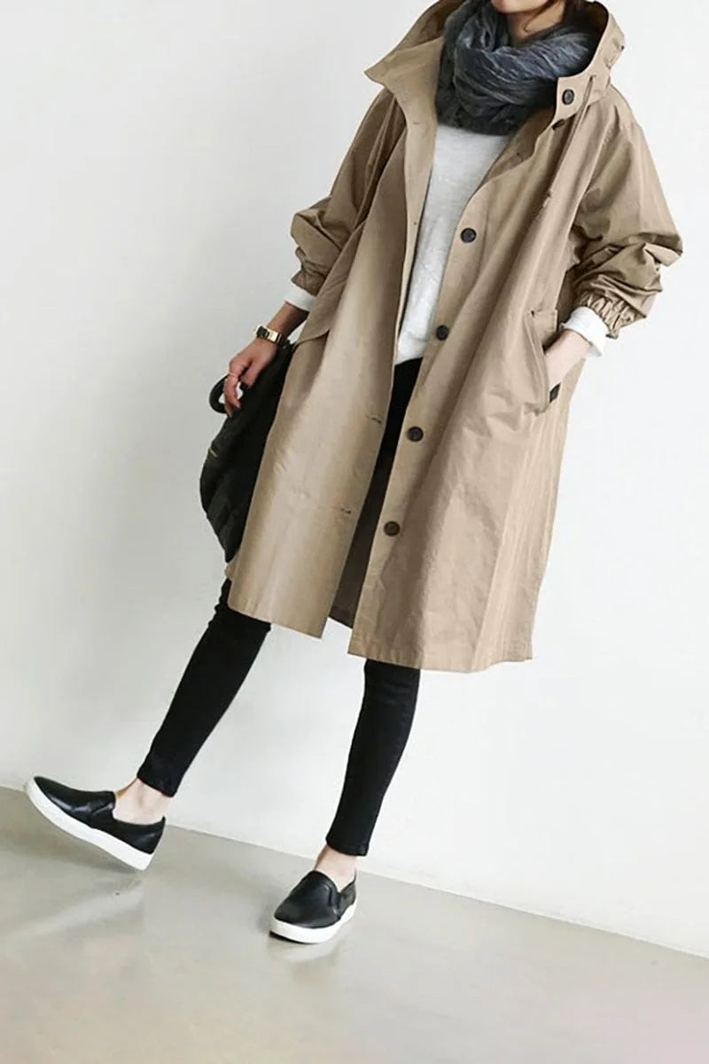 Beige hooded longline coat worn open over a white jumper, paired with black trousers and trainers
