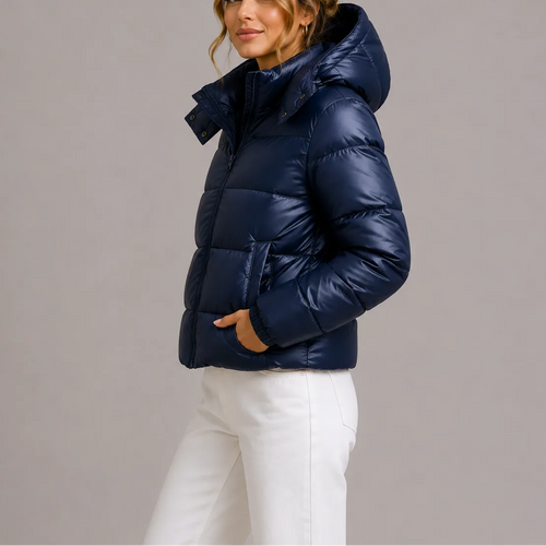 Side view of a navy glossy hooded puffer jacket worn with white wide-leg trousers, hands in front pockets