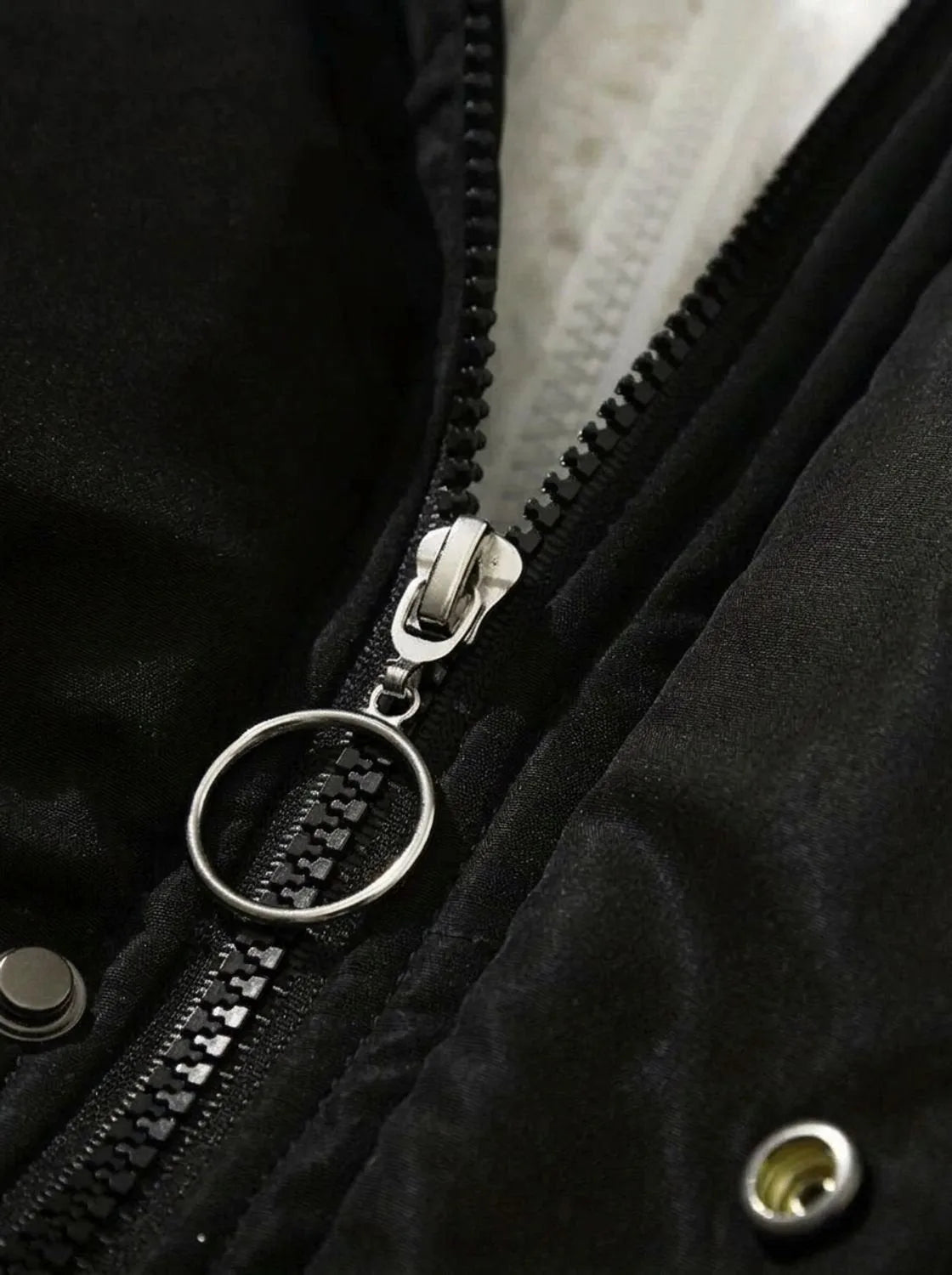 Close-up of black zip pull with silver ring detail and press stud fastening
