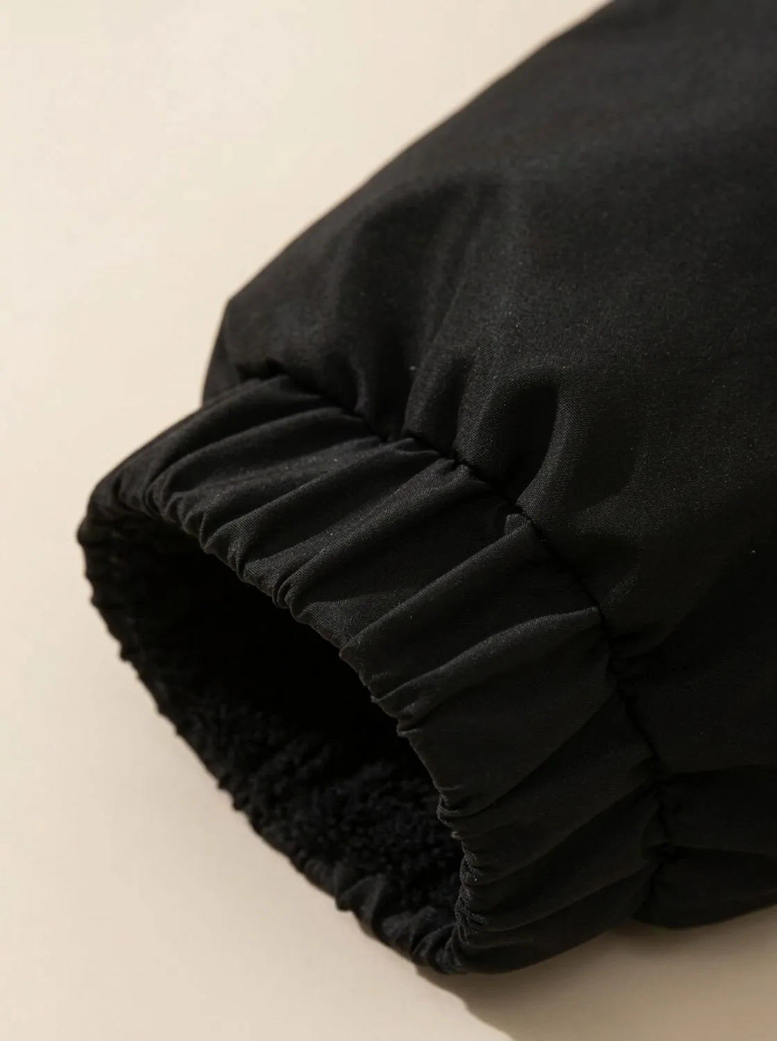 Close-up of elasticated cuff with drawcord toggle on black puffer jacket sleeve