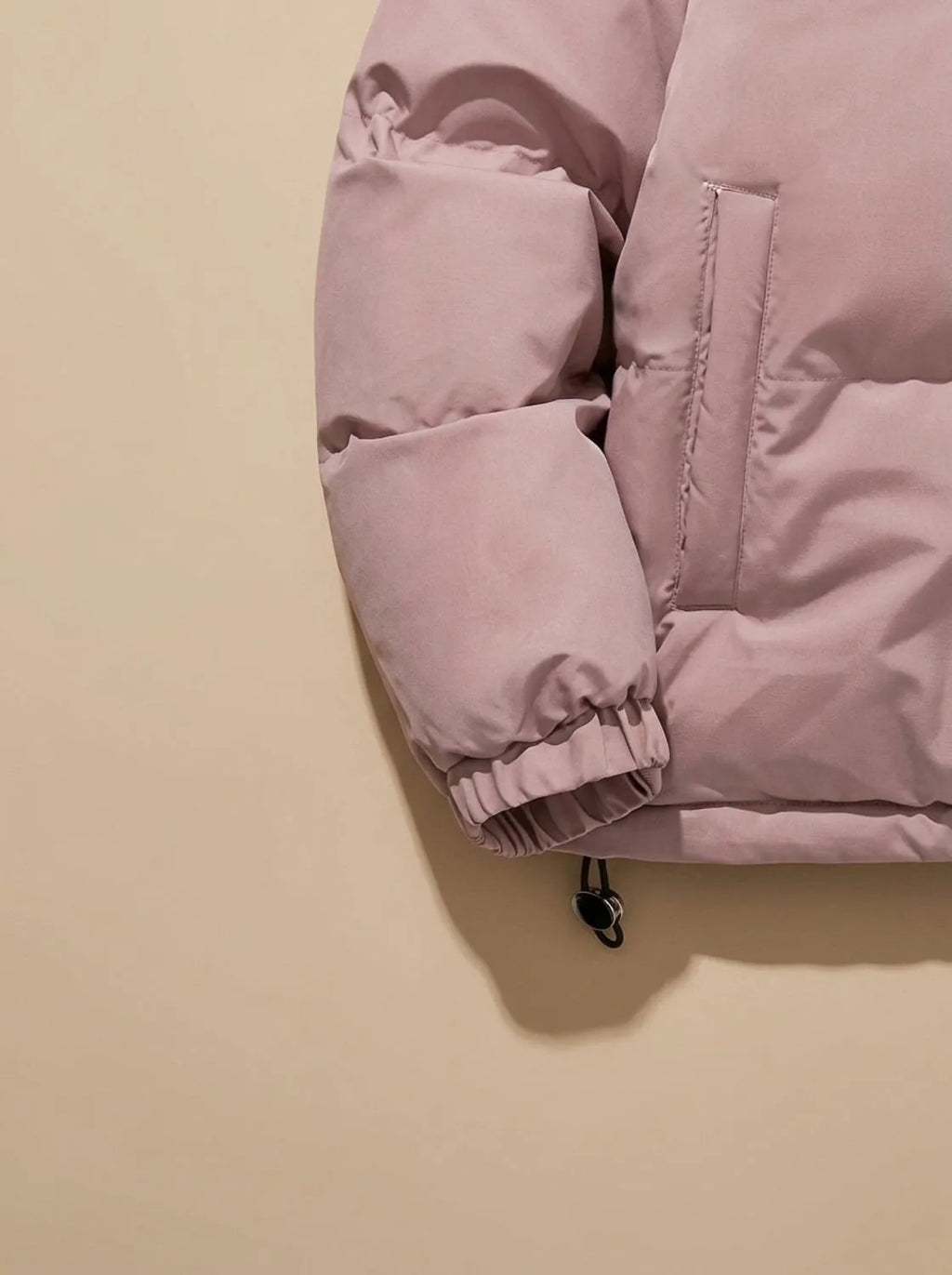 Close-up of pink puffer jacket sleeve cuff, side pocket and drawcord toggle