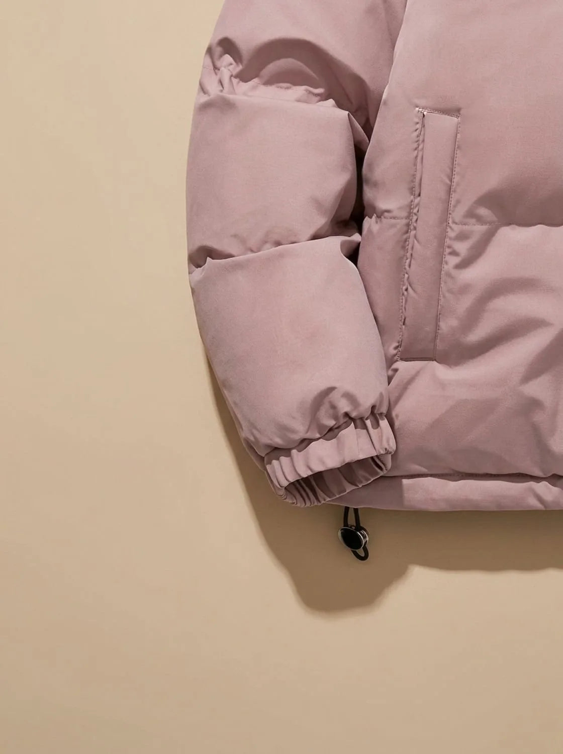 Close-up of pink puffer jacket sleeve cuff, side pocket and drawcord toggle
