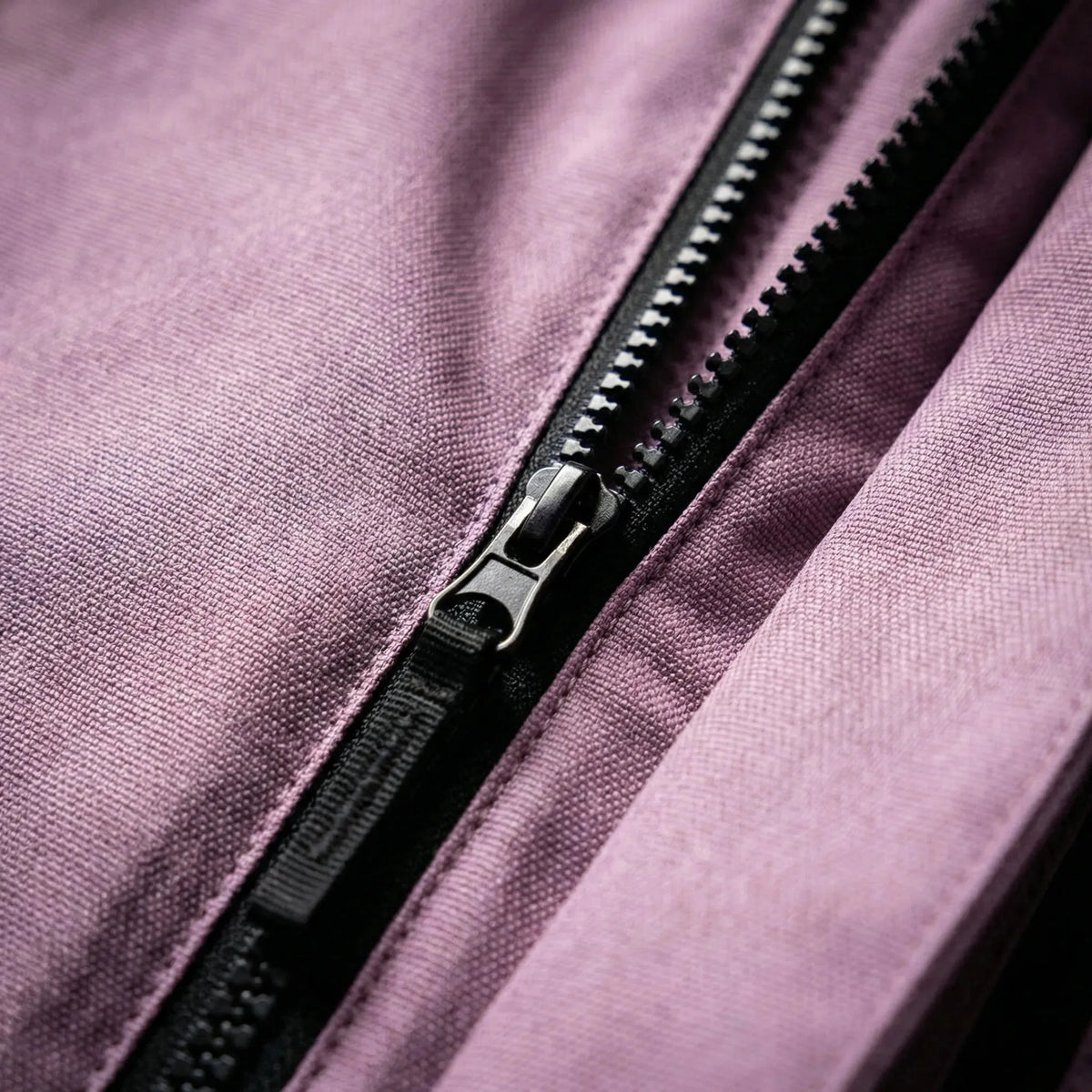 Close-up of the lilac fabric and matte black zip pull on the jacket's centre front closure