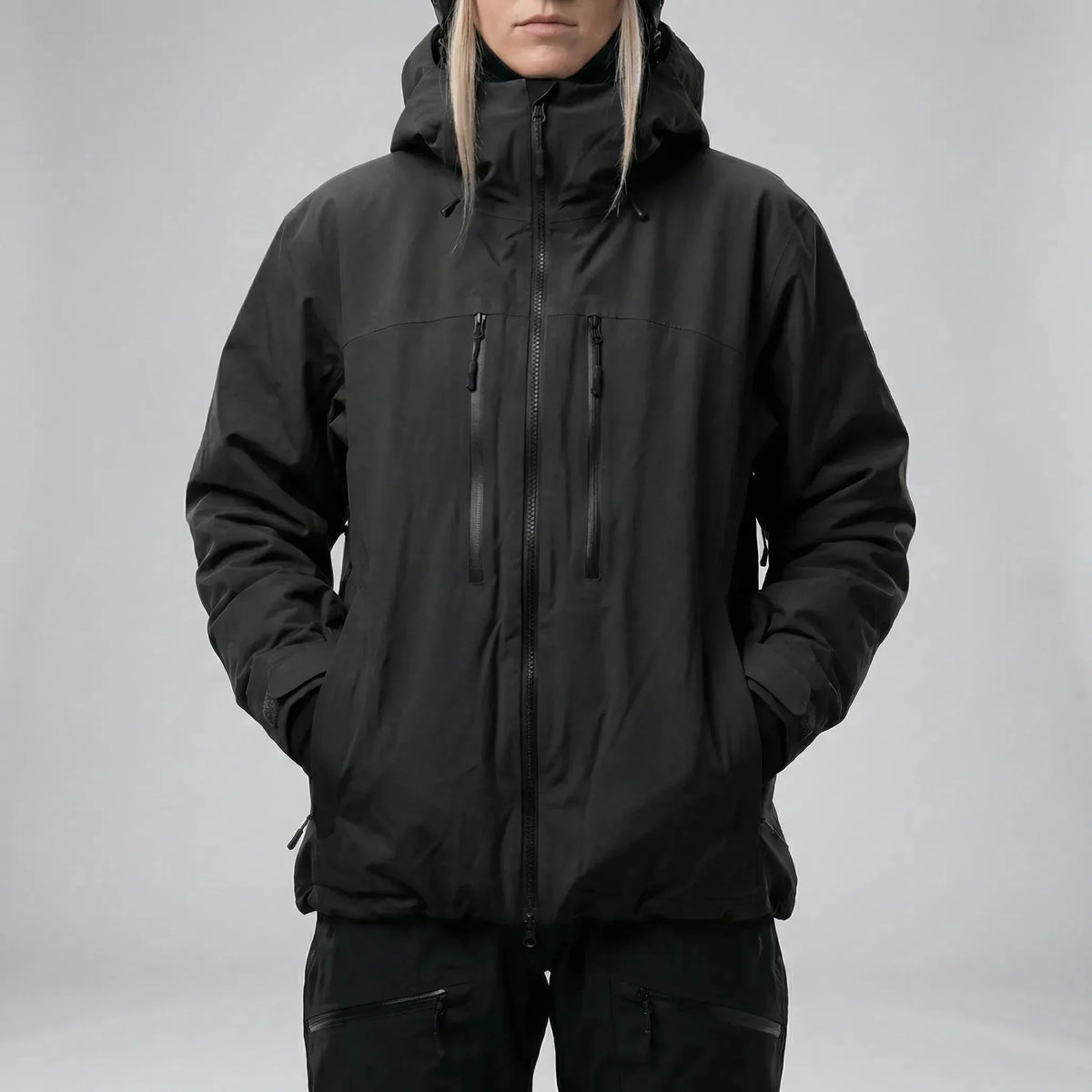 Front view of the same jacket style in black, hands in side pockets, worn over black ski trousers