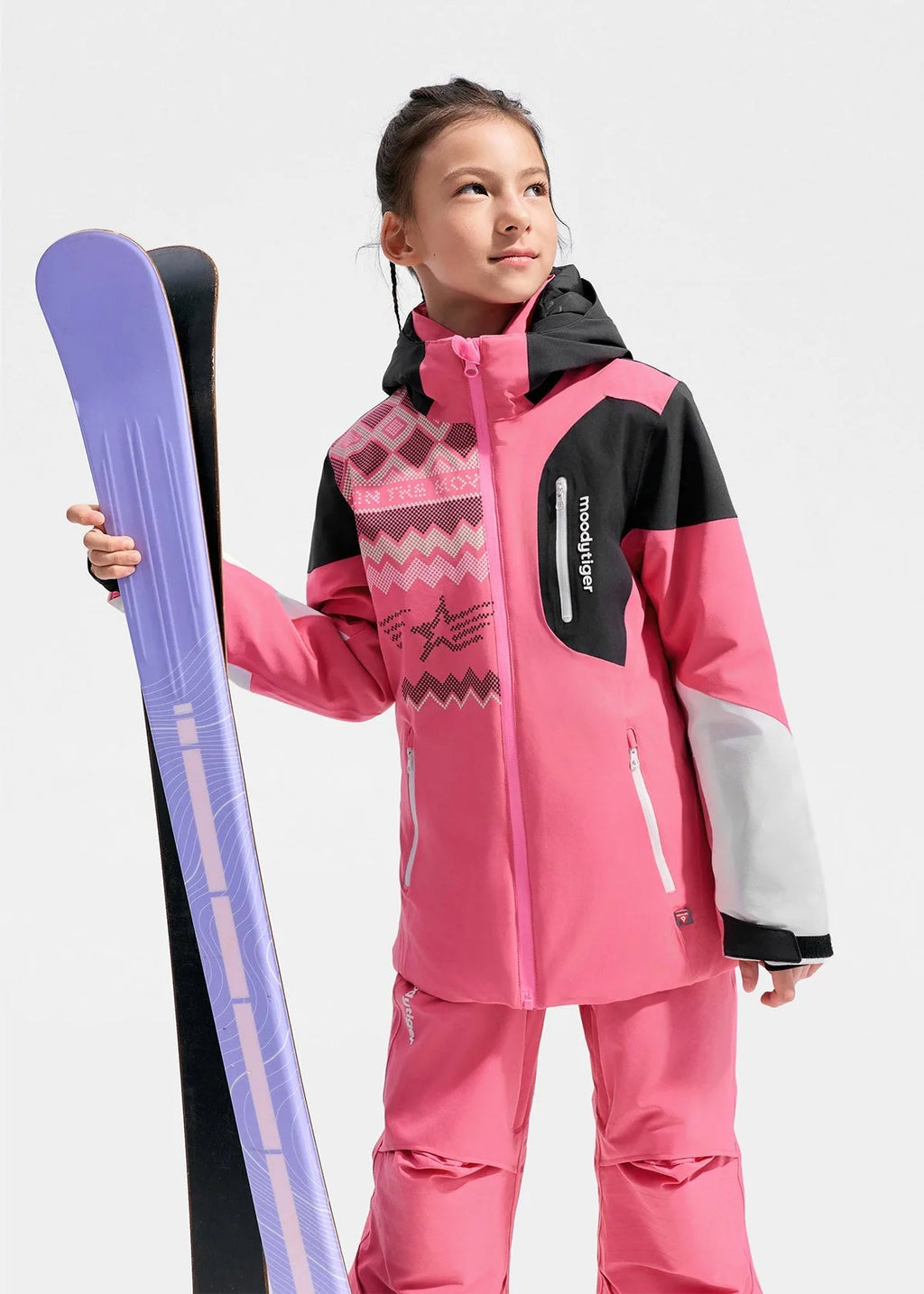 Girl in pink and black colour-block ski jacket holding purple skis over her shoulder against a grey backdrop