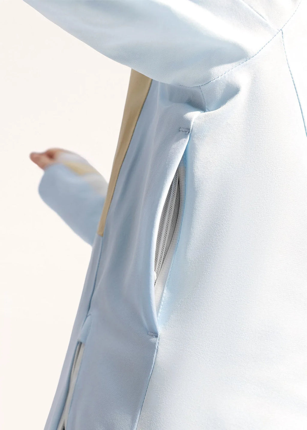 Close-up of hands in white knit cuffs framing the pale blue jacket's tan chest pocket and zip pull