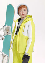 Boy wearing a lime yellow and white ski jacket with grey beanie, standing beside a teal snowboard