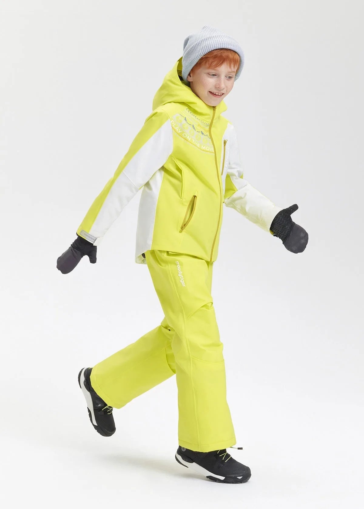 Side view of the boy walking in the lime yellow ski jacket, showing the relaxed fit and printed graphic on the chest