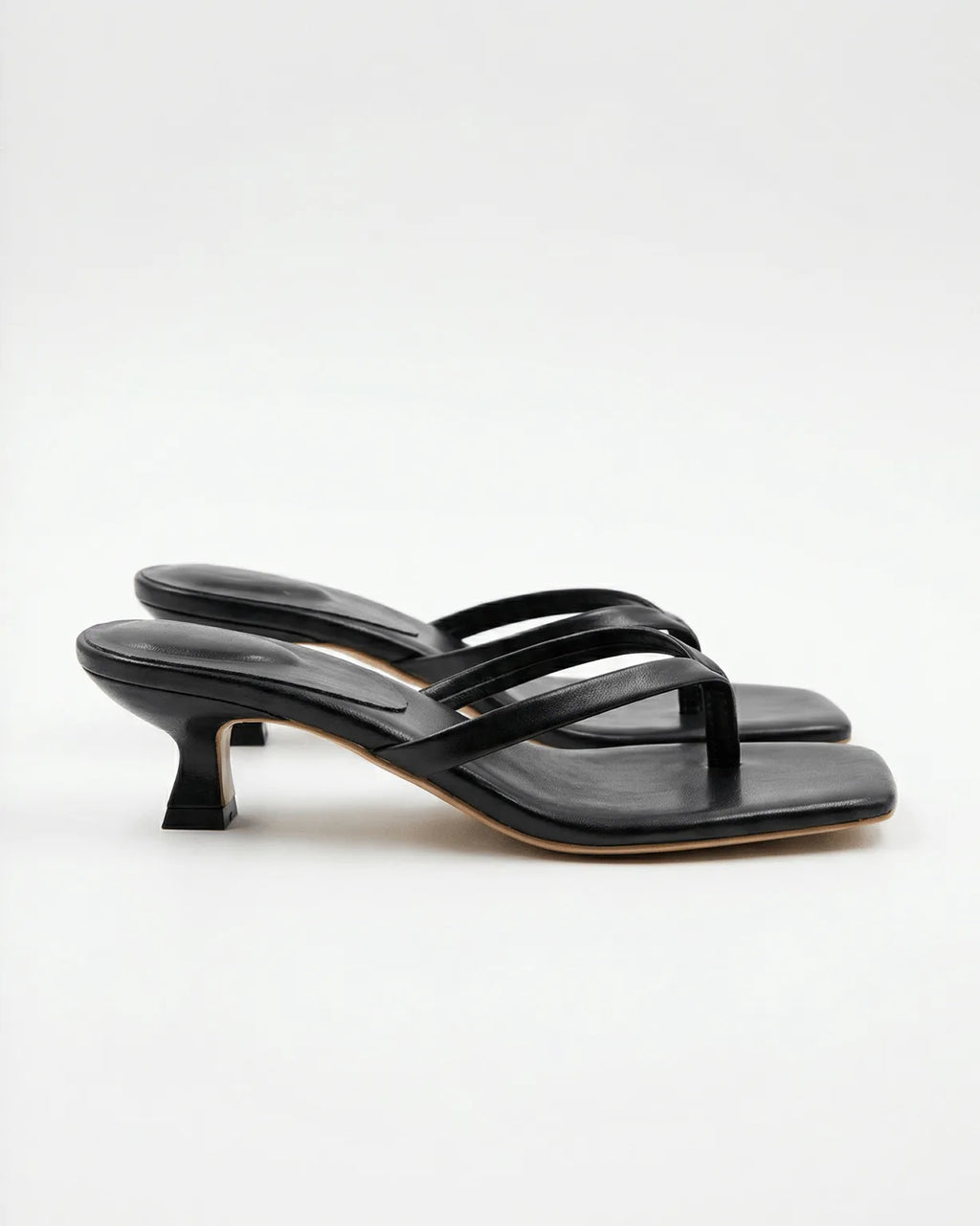 Side view of black leather kitten-heel sandal with square toe and thin crossover straps against a white background