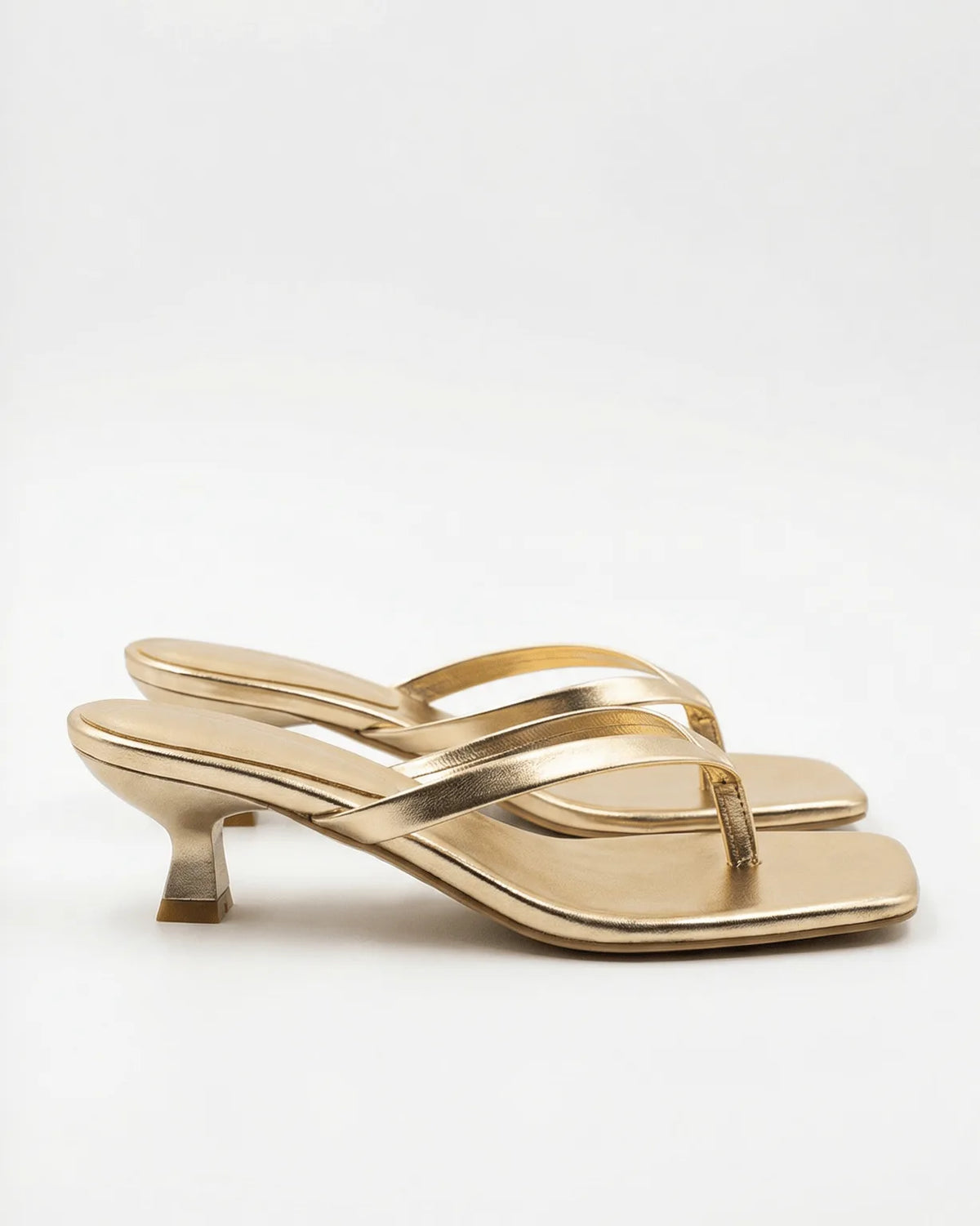 Gold metallic leather thong sandal with sculptural spool heel and square toe, side profile