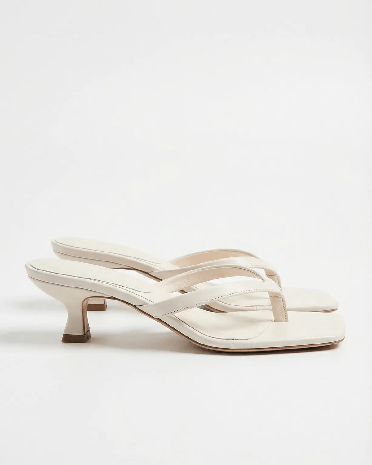 Ivory leather flip-flop style sandal with slim straps and flared spool heel, side angle