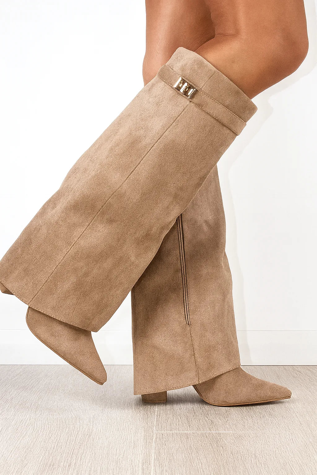 Side view of beige suede knee-high foldover boots with gold buckle detail and pointed toe, worn on bare legs