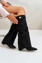 Seated pose showing black suede knee-high foldover boots with gold hardware, paired with gold jewellery
