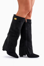 Side view of black suede knee-high foldover boots with visible zip and block heel on bare legs