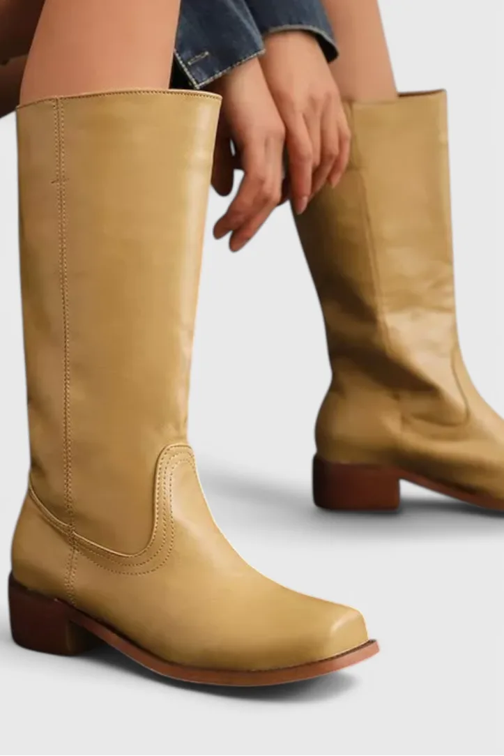 Close-up side view of a knee-high yellow leather boot with stitched panel detail and a stacked wooden heel