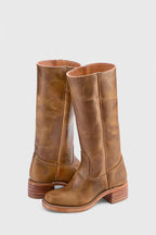 Back three-quarter view of weathered tan leather knee-high boots highlighting the natural grain and stacked heel