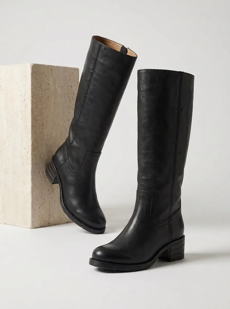 Pair of black leather knee-high boots with block heel, one leaning against a stone block, side view