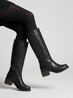 Close-up side view of black leather knee-high boots on model's legs, showing stacked block heel detail