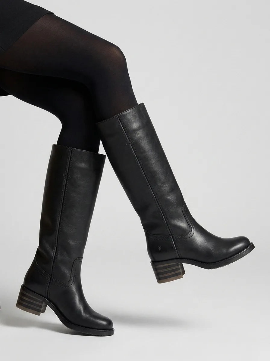 Close-up side view of black leather knee-high boots on model's legs, showing stacked block heel detail