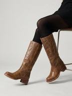 Pair of brown leather knee-high boots leaning against a stone block, showing worn-in leather texture