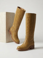 Woman seated wearing brown leather knee-high boots with black tights, close view of stacked heel
