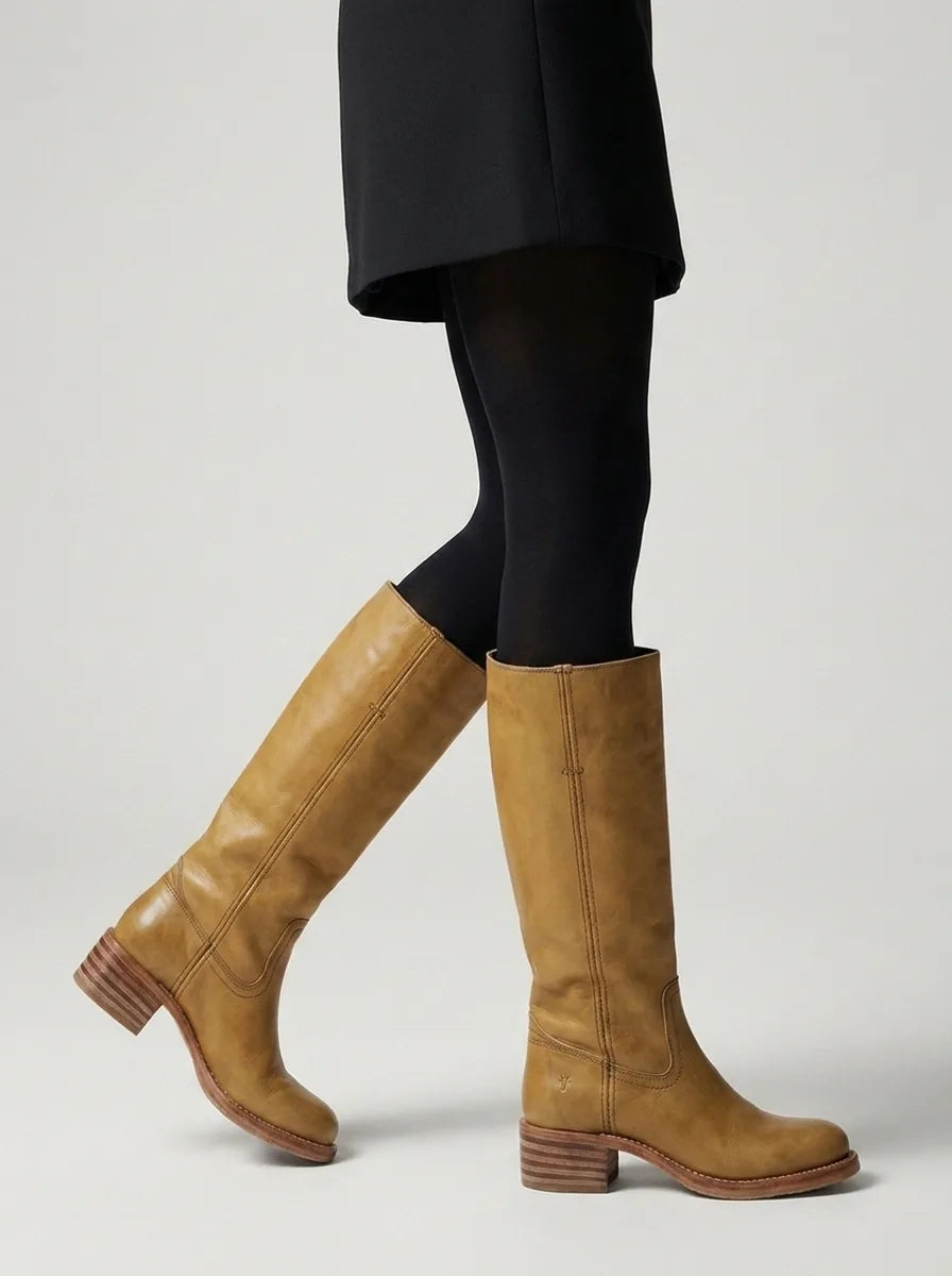 Pair of light tan leather knee-high boots standing upright against a stone block, front view