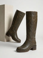 Woman seated wearing mustard yellow leather knee-high boots, showing stacked wooden-look heel