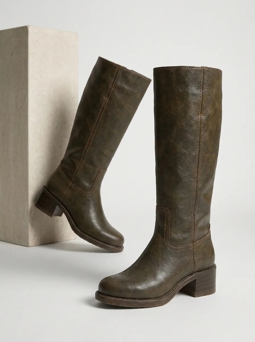 Woman seated wearing mustard yellow leather knee-high boots, showing stacked wooden-look heel