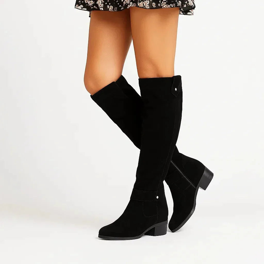 Black suede knee-high boots styled with a floral skirt, showing the back heel and ankle strap detail