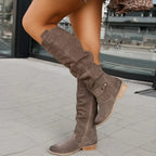 Taupe suede knee-high boots in profile, highlighting the slouchy ruched leg and stacked wooden-look heel