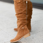 Tan suede knee-high boots shown close up, focusing on the buckle strap, pull tab and rounded toe