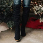 Black suede knee-high boots worn with jeans, rear view showing the ruched shaft and heel construction