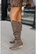 Taupe suede knee-high slouch boots worn outdoors, side profile showing the low block heel and pointed toe