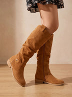 Close-up profile of tan brown suede knee-high boots highlighting the pointed toe and block heel